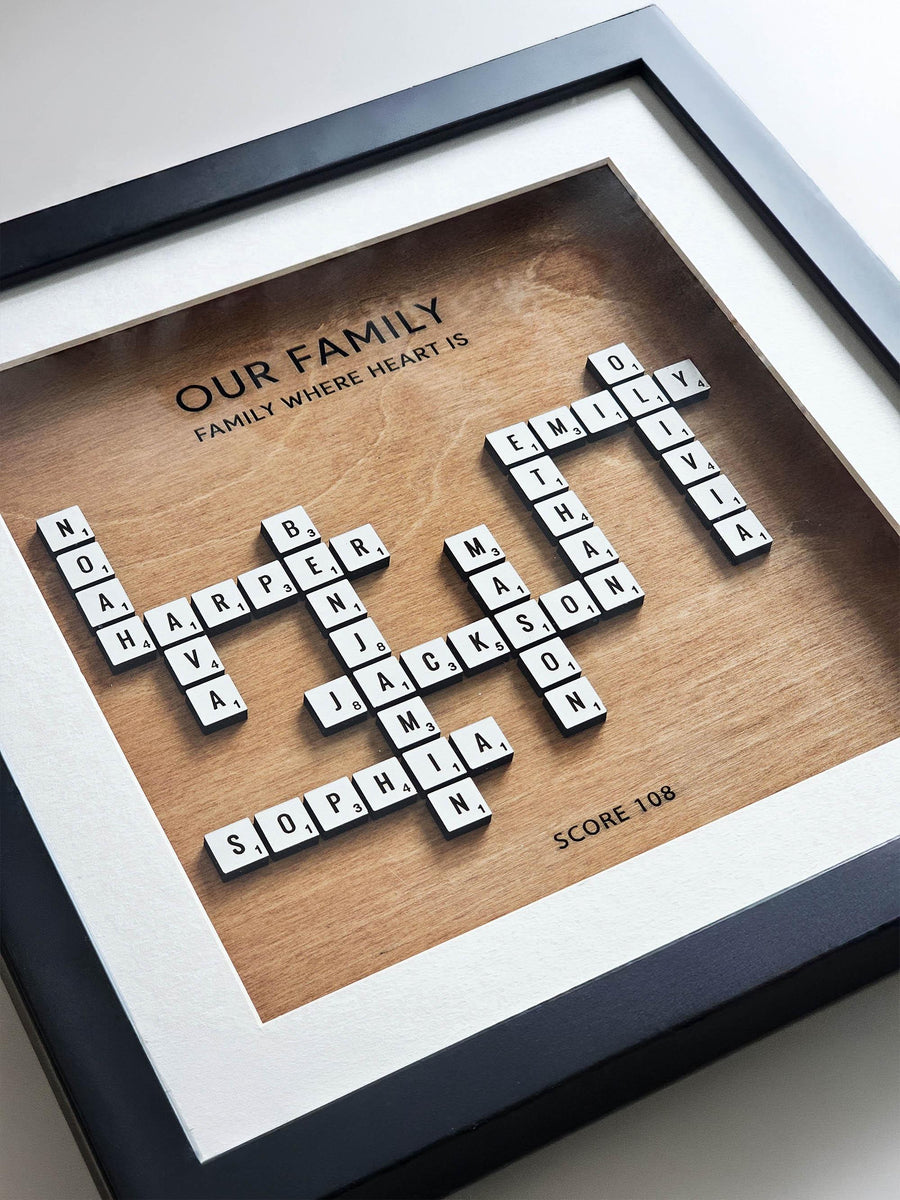 Close-up of the crossword family name frame: white letter tiles with point numbers on a hazelnut wood background, titled Our Family, inside a black frame.