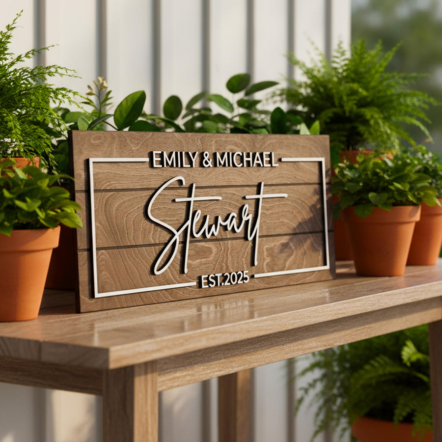 Family name sign reading Emily & Michael Stewart, Est. 2025 in raised white letters, on a wooden table among potted plants.
