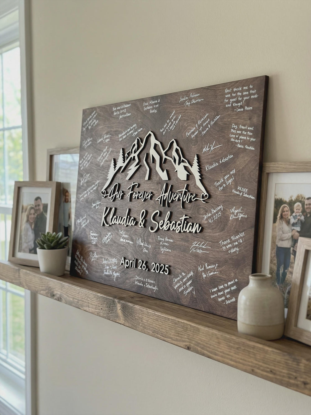Signed forest mountain guest book sign displayed on a home shelf beside framed photos.