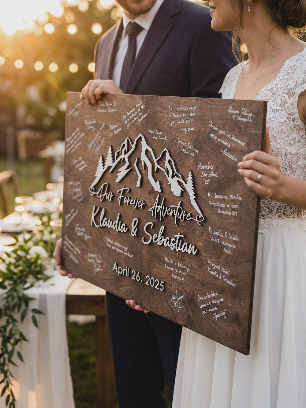 Bride and groom holding the signed forest mountain guest book board with Our Forever Adventure, their names and date in raised white letters.