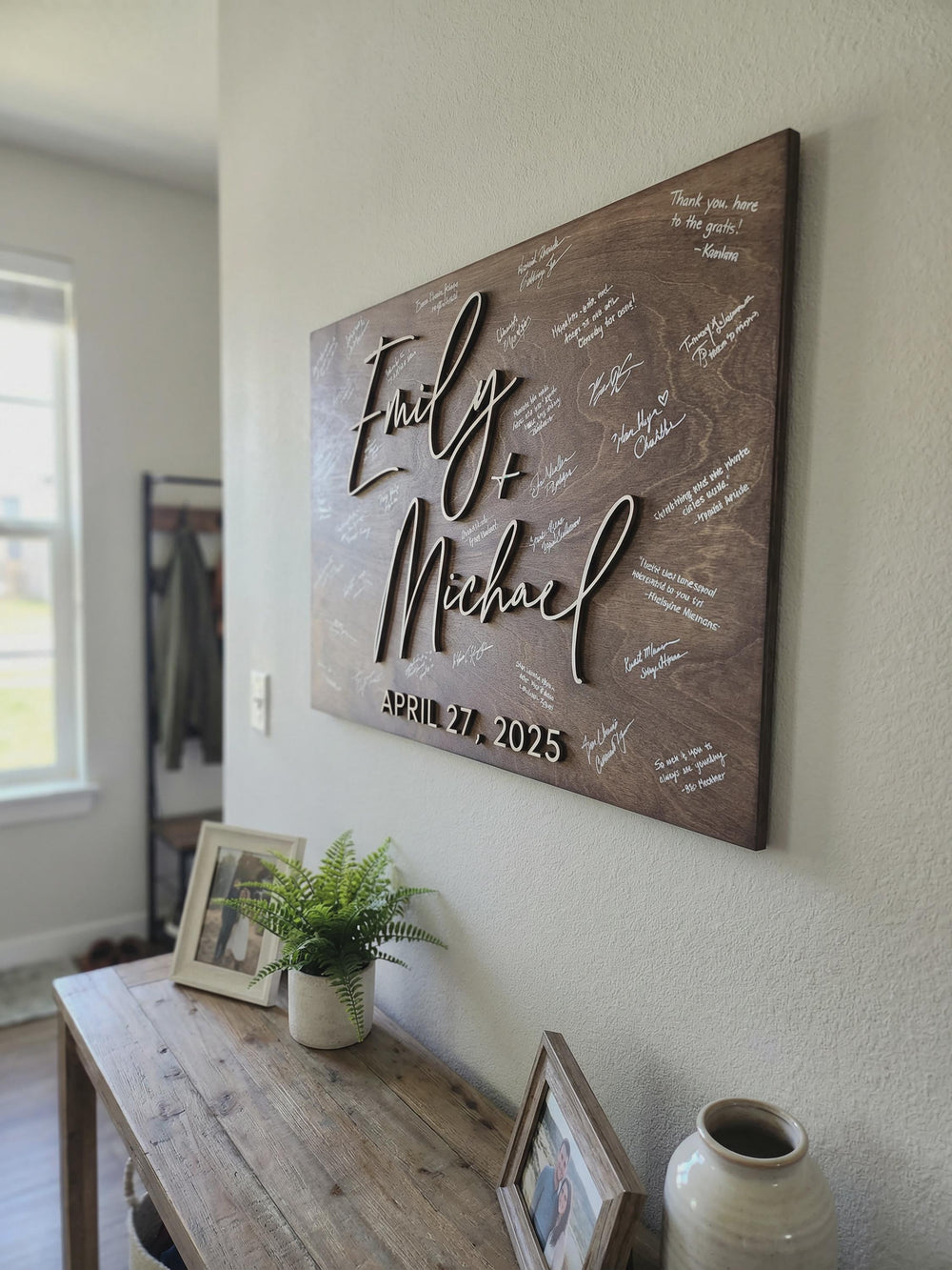 Personalized wedding guest book alternative displayed as wall decor, rustic dark wood 3D guestbook sign with custom names, wedding date, and white guest signatures in home entryway.