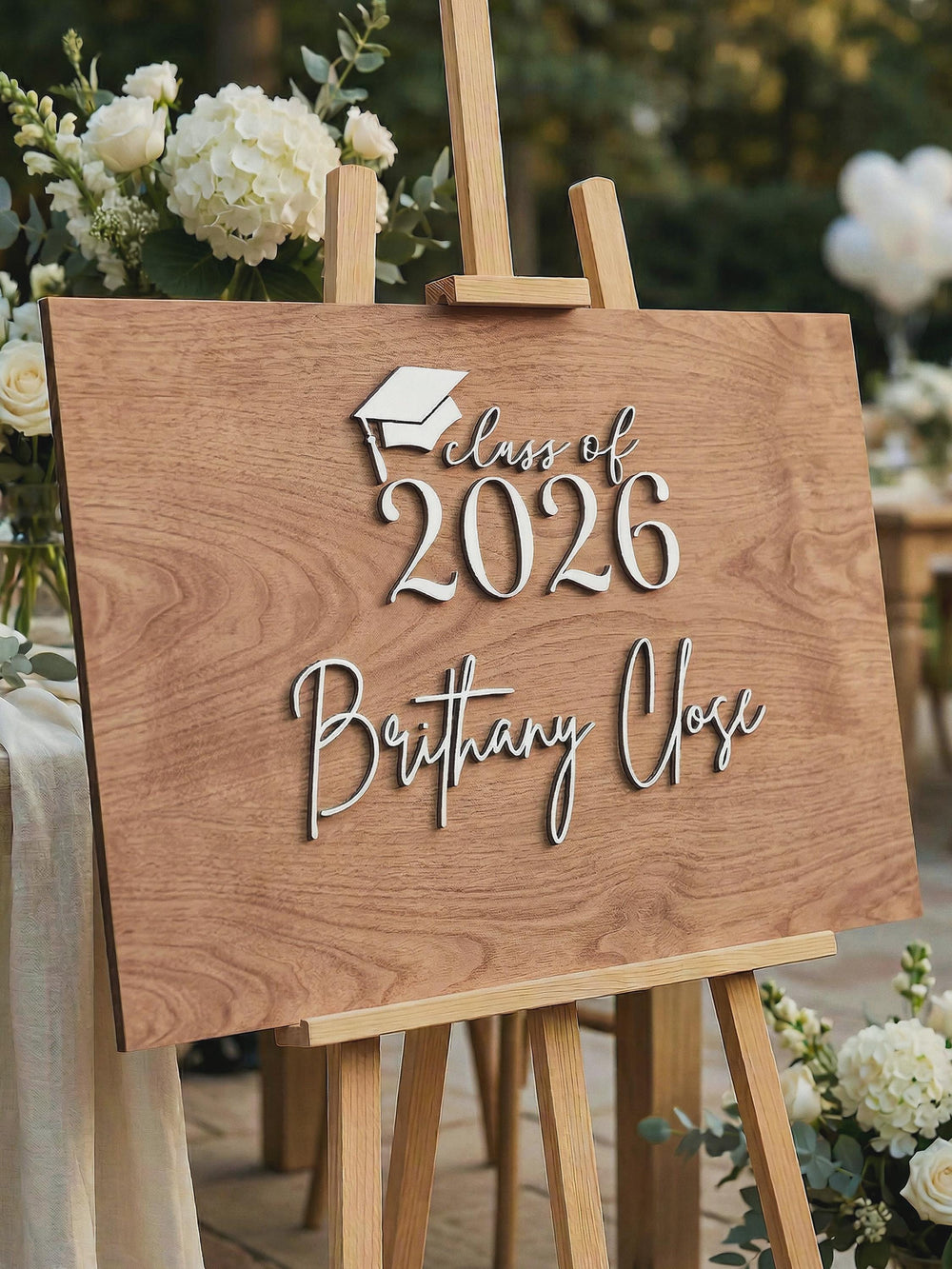 The Class of 2026 sign with the name Brittany Close in raised 3D letters on a wooden easel, before the guests sign it.
