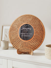 Wooden song record with engraved lyrics in a spiral and a dark mirror center with white lettering, standing on its wooden display stand