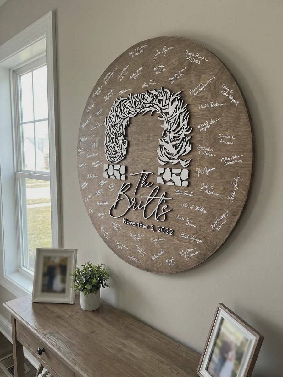A round wooden Jackson Hole arch guest book sign covered in white guest signatures, hanging on a hallway wall above a console table.