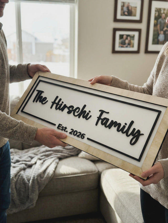 Couple holding a Natural wood framed sign reading The Hirschi Family Est. 2026 in raised black script.