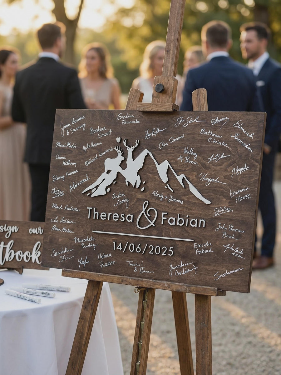 Personalized mountain wedding guest book alternative displayed on a wooden easel, featuring raised deer and mountain details, couple names, wedding date, and guest signatures.