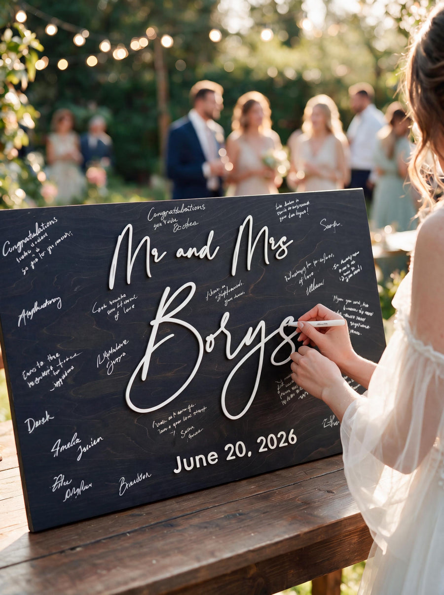 Black Mr and Mrs wedding guest book sign with the couple's last name and wedding date in raised white script, signed by guests.