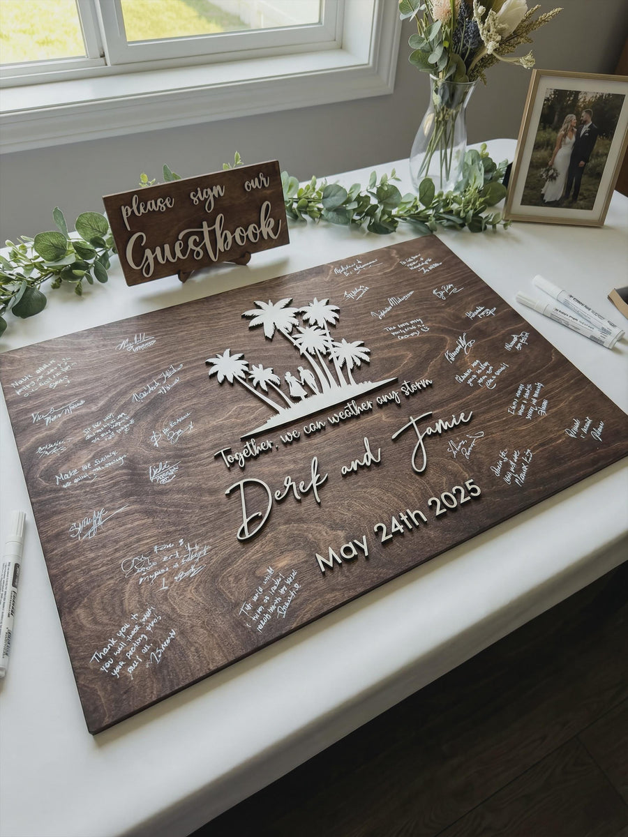 Jacobean rectangular guest book board on a welcome table, signatures filling in around a raised palm tree island, Together, we can weather any storm, Derek and Jamie and May 24th 2025, with the Please Sign Our Guestbook mini sign.