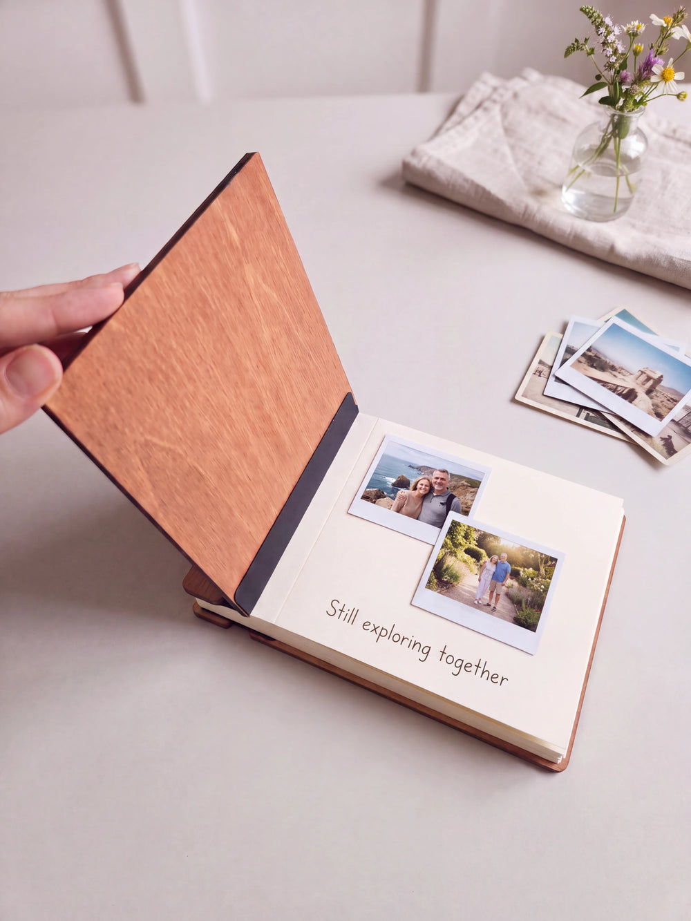 A hand lifts the Hazelnut album cover. Two couple travel photos sit on a cream page above the handwritten note 