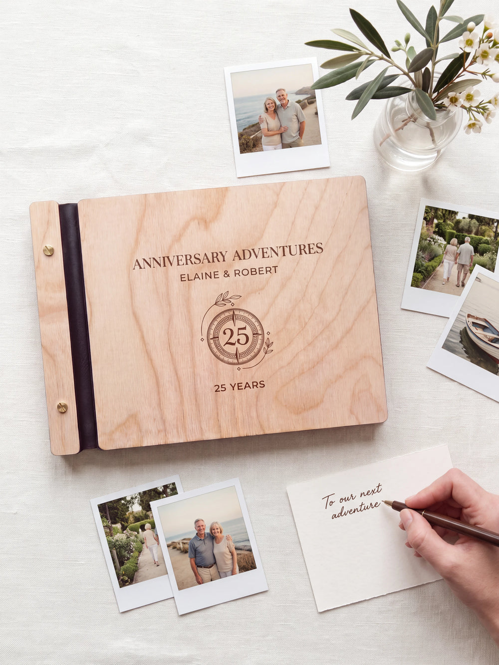 A Natural wooden album showing a circular 25-year anniversary emblem rests beside a separate gift card. A hand writes 