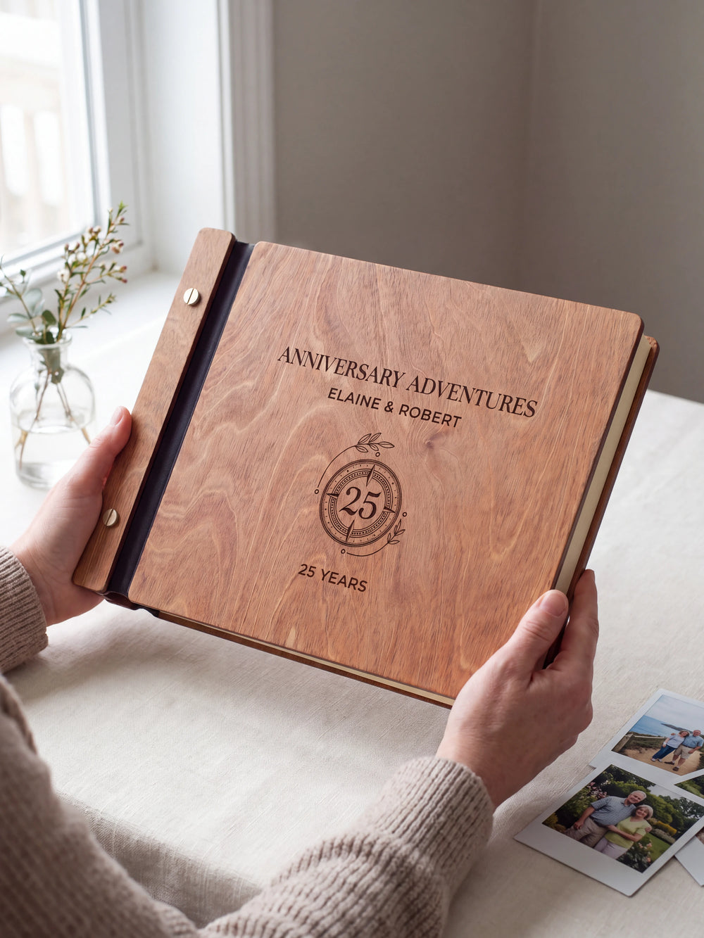 Hands hold the Hazelnut wooden album near a window. The full cover displays a circular 25-year anniversary emblem in dark engraving, with personalized lettering and a black binding strip.