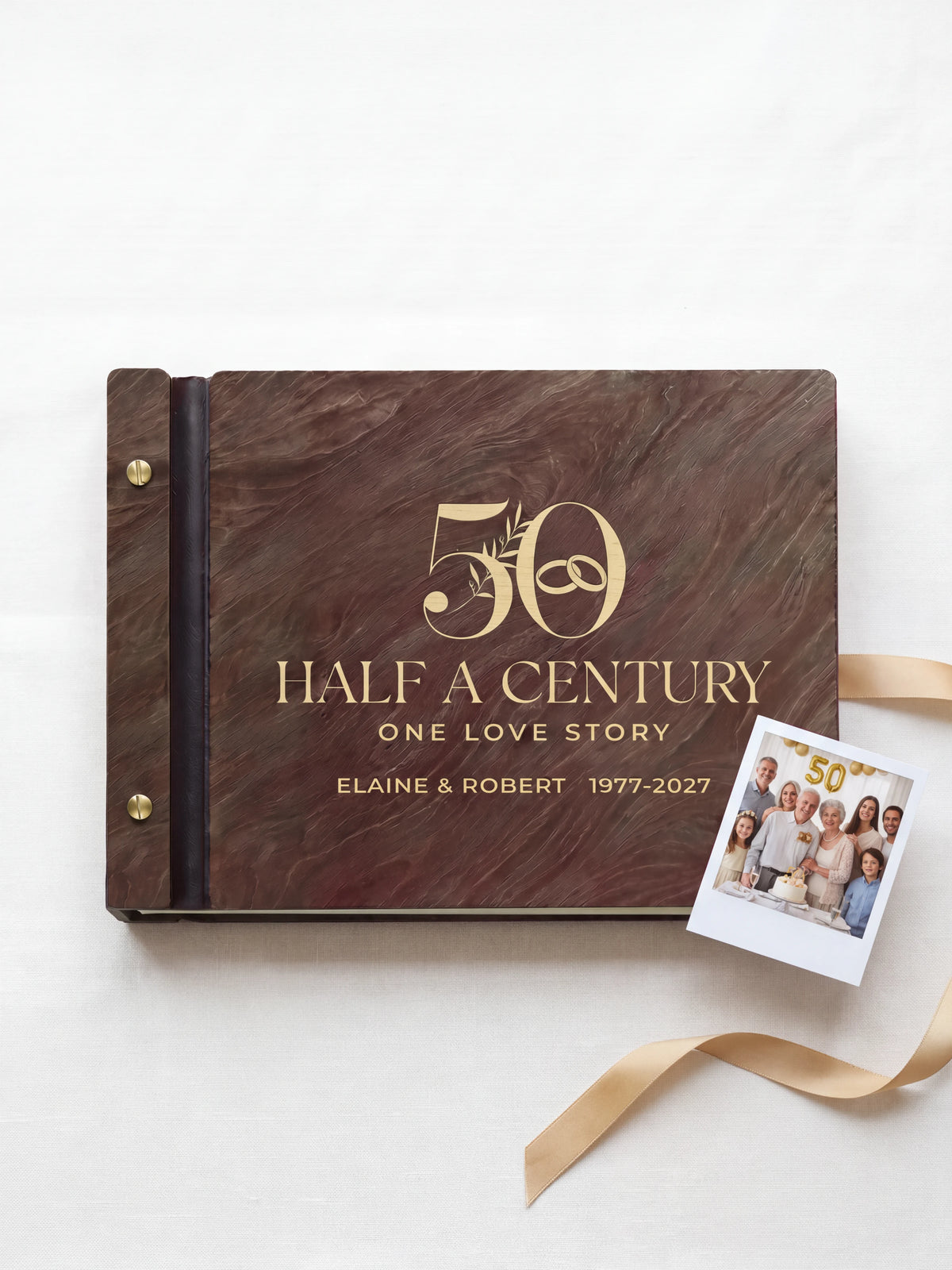 Jacobean wood 50th anniversary photo memory book lying flat on ivory linen, the cover engraved with “50”, “HALF A CENTURY, ONE LOVE STORY” and “ELAINE & ROBERT 1977-2027”; two gold-tone screws along the black vegan leather spine