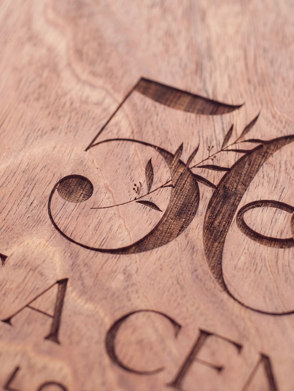 Close-up of the laser engraving on Hazelnut wood: a large number 50 with interlocking wedding rings and leaves and the personalized text against the visible wood grain
