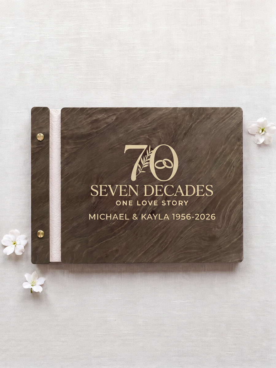 Jacobean wooden photo album with cream laser engraving of a large 70 with a botanical sprig and interlocking wedding rings. The closed book rests on pale linen with ivory binding and gold screws.