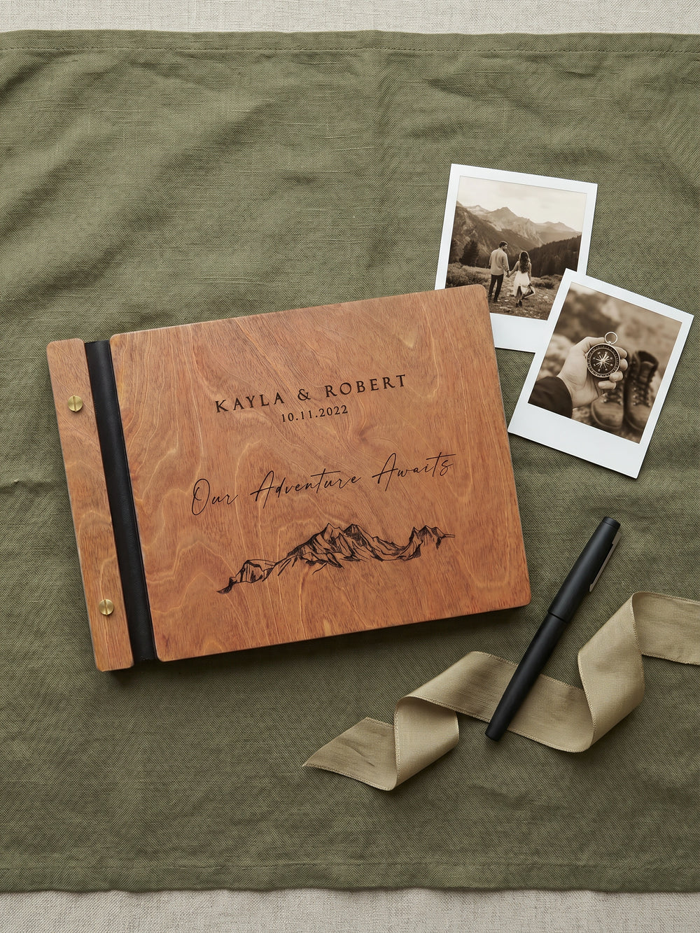 Hazelnut wood Our Adventure Awaits photo guest book on olive linen with two sepia instant photos, a pen and a ribbon
