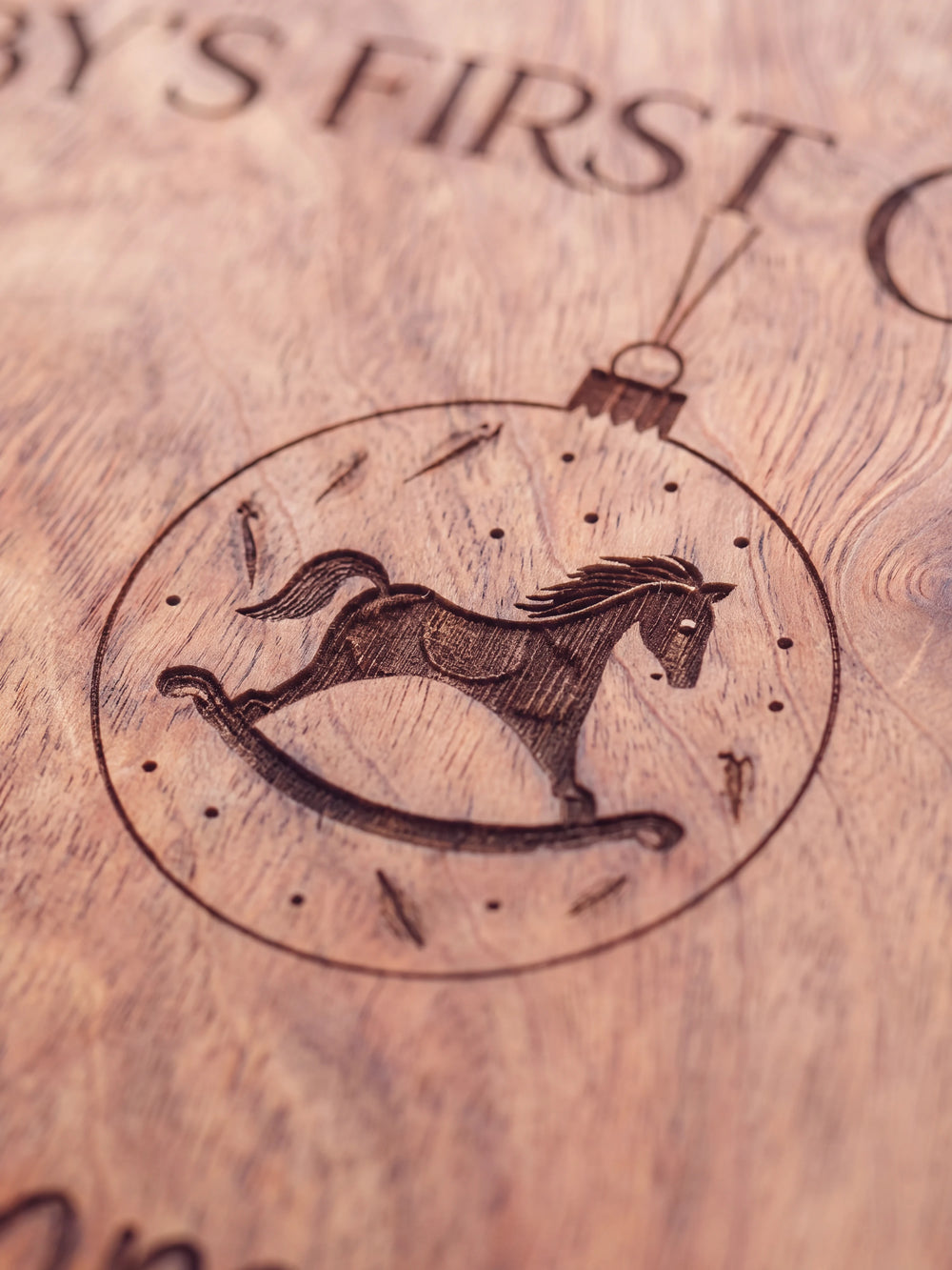 Close-up of the laser engraving on Hazelnut wood: a hanging ornament with a rocking horse inside and the personalized text against the visible wood grain