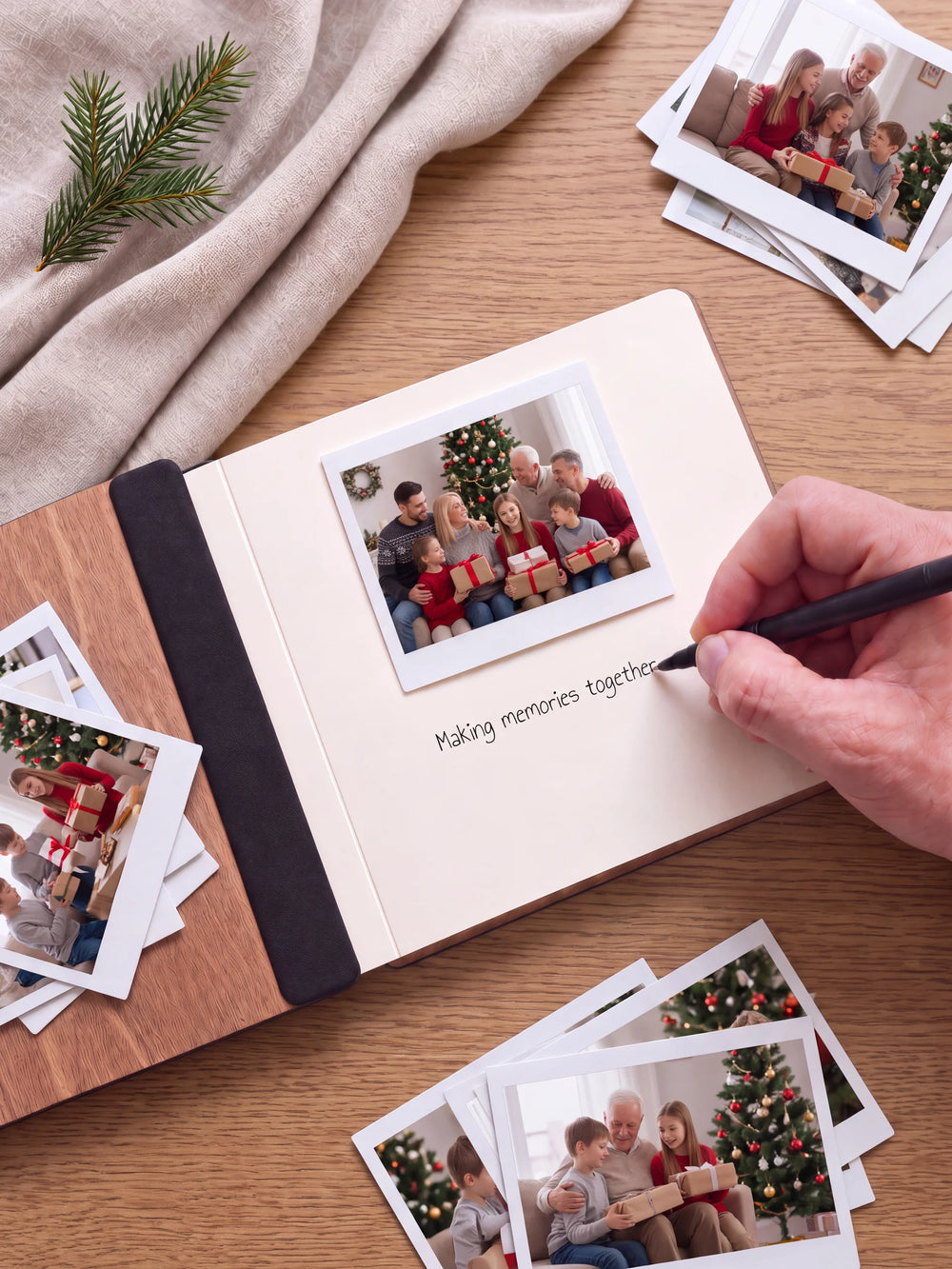 An open Hazelnut album with a photograph on a cream page. A hand writes a memory beneath it; a flat black fabric strip runs along the inner wooden cover.