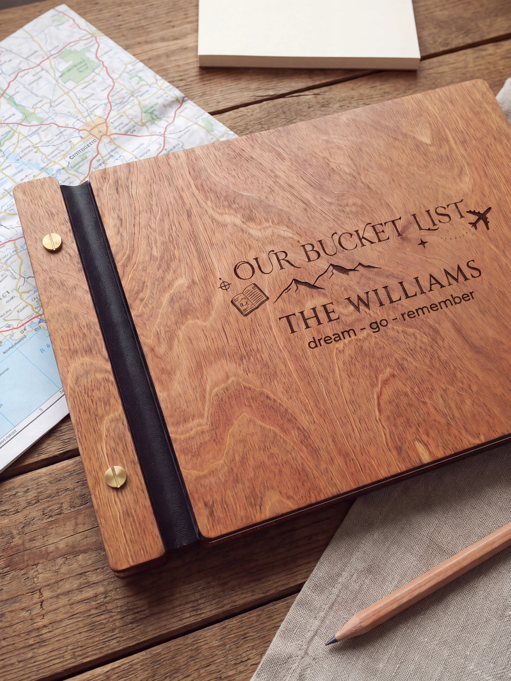 Close-up of mountains, a passport and an airplane engraved in dark brown on the Hazelnut wooden cover, showing the fine artwork and surrounding wood grain.