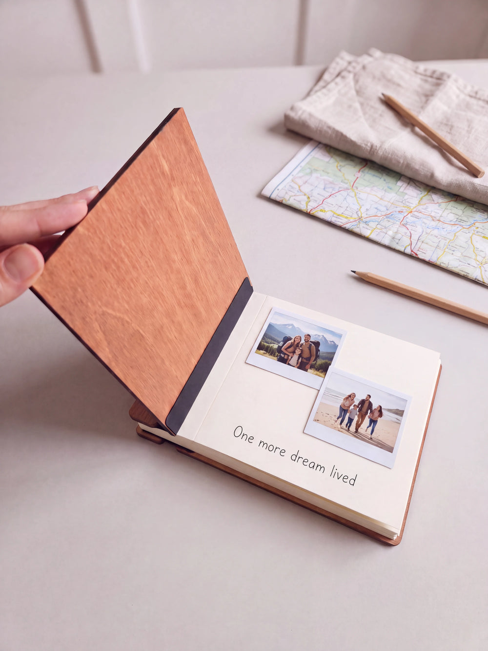 A hand lifts the Hazelnut album cover. Two family vacation photos sit on a cream page above the handwritten note 