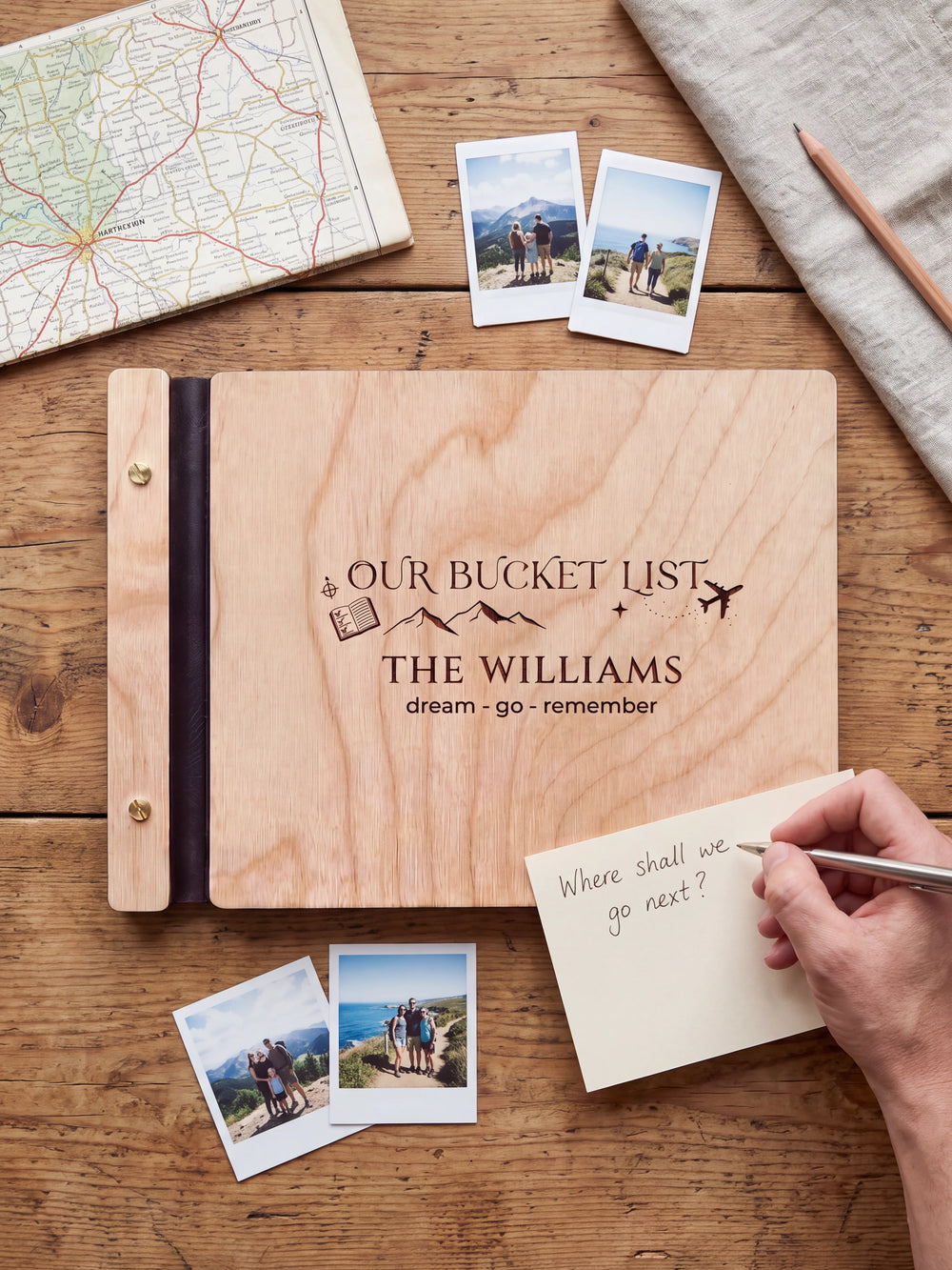 A Natural wooden album showing mountains, a passport and an airplane rests beside a separate gift card. A hand writes 