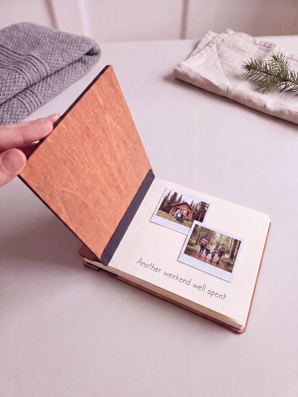 A hand lifts the Hazelnut album cover. Two cabin and woodland photos sit on a cream page above the handwritten note 