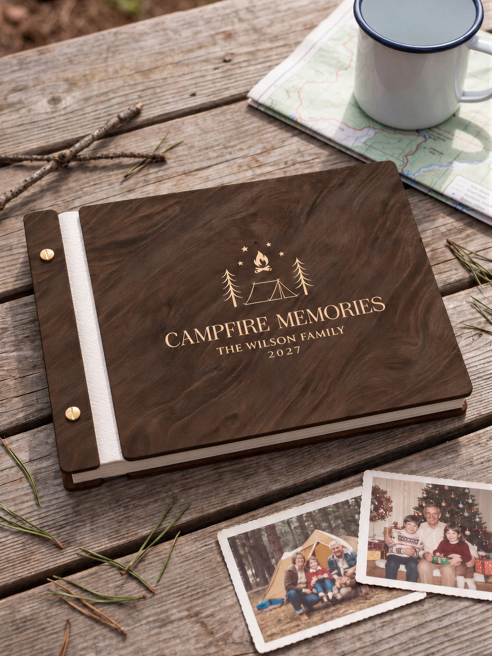 Jacobean wooden album with cream laser engraving of tent, campfire, pine trees and stars. The full personalized cover rests on a styled surface, with ivory binding and gold screws.
