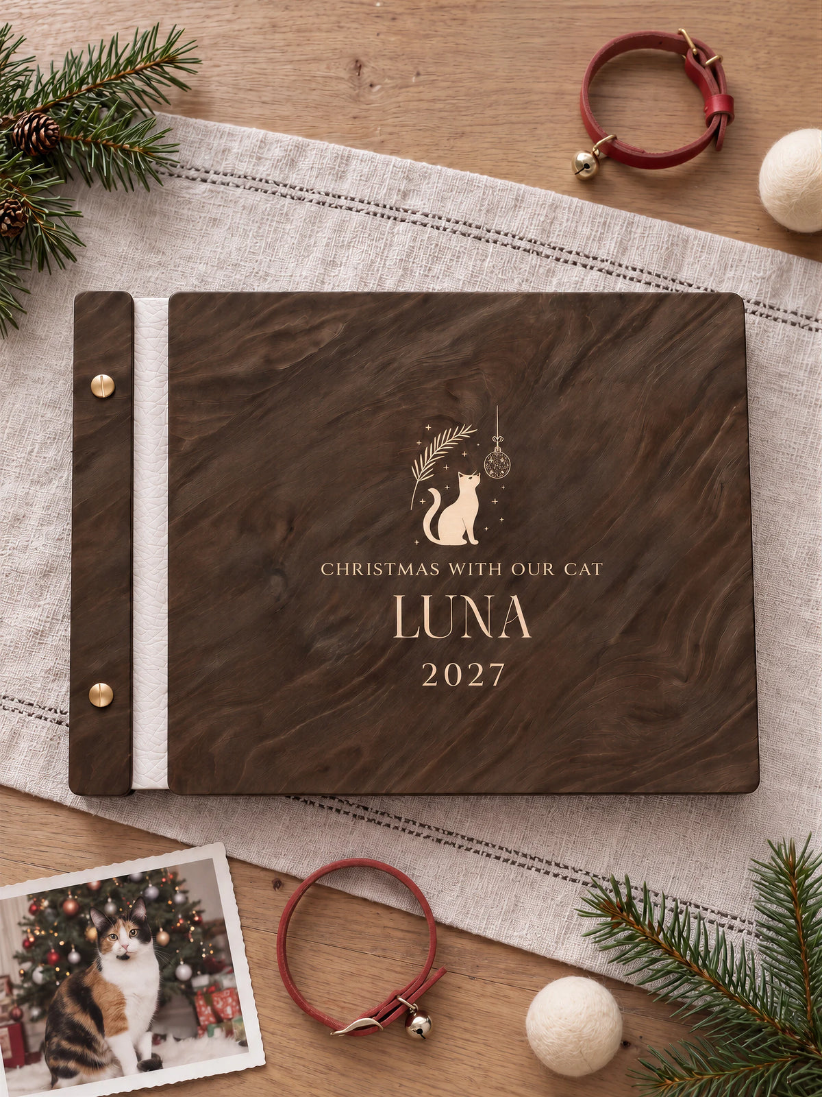Jacobean wooden album with cream laser engraving of cat silhouette, hanging ornament and foliage. The full personalized cover rests on a styled surface, with ivory binding and gold screws.