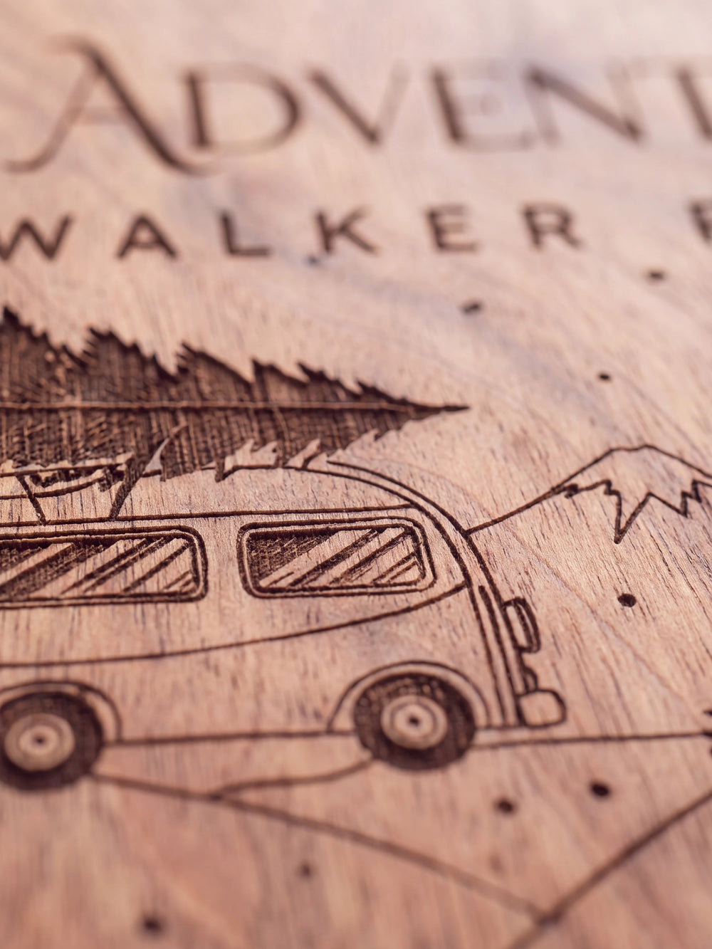 Close-up of the laser engraving on Hazelnut wood: a camper van carrying a Christmas tree among snowy pines and the personalized text against the visible wood grain