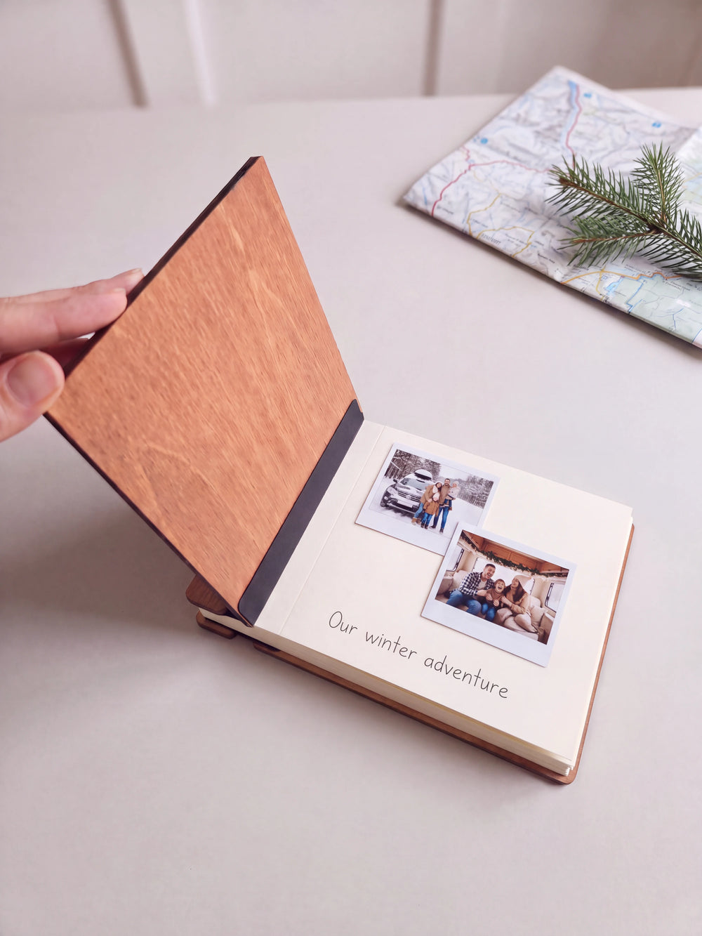 The Hazelnut Christmas Adventures photo book open on a table with instant photos and a short handwritten note on a cream page; the black hinge strip is visible