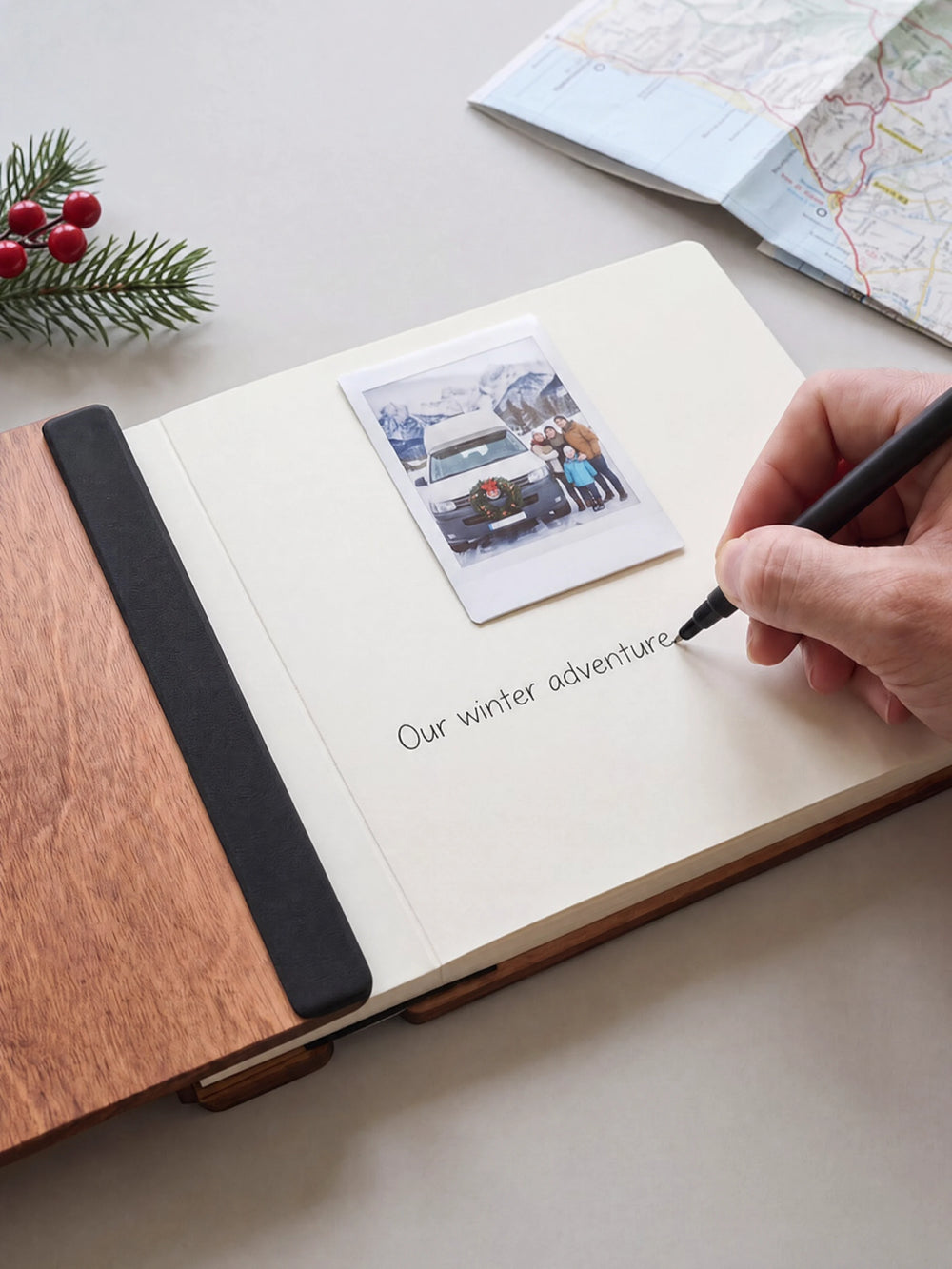 A hand writing a note in fine black pen beneath an instant photo on the cream page of the open Hazelnut Christmas Adventures photo book