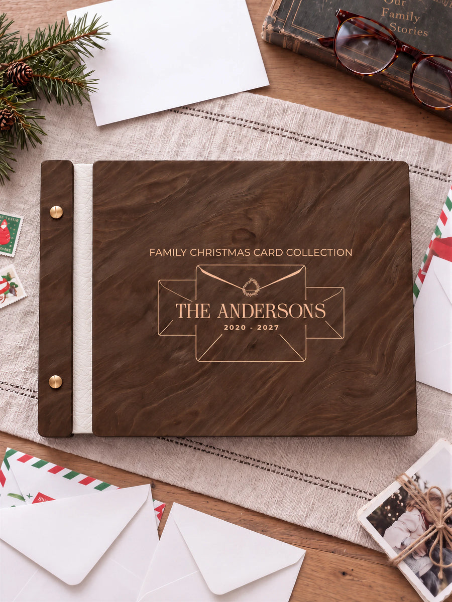 Jacobean wooden album with cream laser engraving of three envelopes and a tiny wreath. The full personalized cover rests on a styled surface, with ivory binding and gold screws.