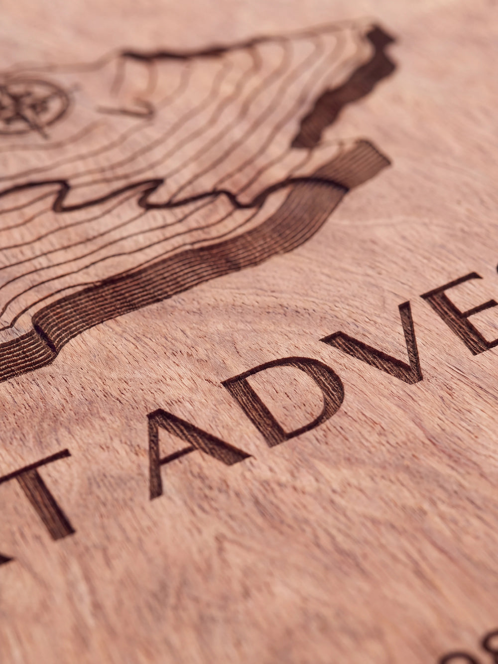 Close-up of the laser engraving on Hazelnut wood: a topographic mountain map with a compass and the personalized text against the visible wood grain