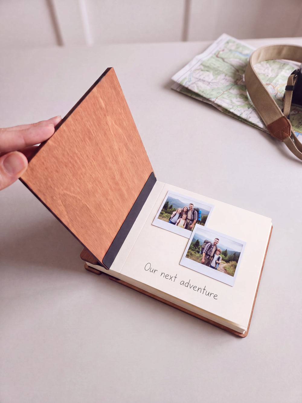 The Hazelnut Dad's Greatest Adventures photo book open on a table with instant photos and a short handwritten note on a cream page; the black hinge strip is visible