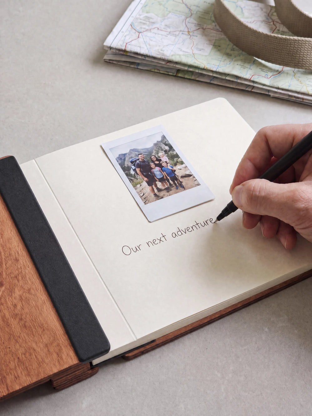 A hand writing a note in fine black pen beneath an instant photo on the cream page of the open Hazelnut Dad's Greatest Adventures photo book