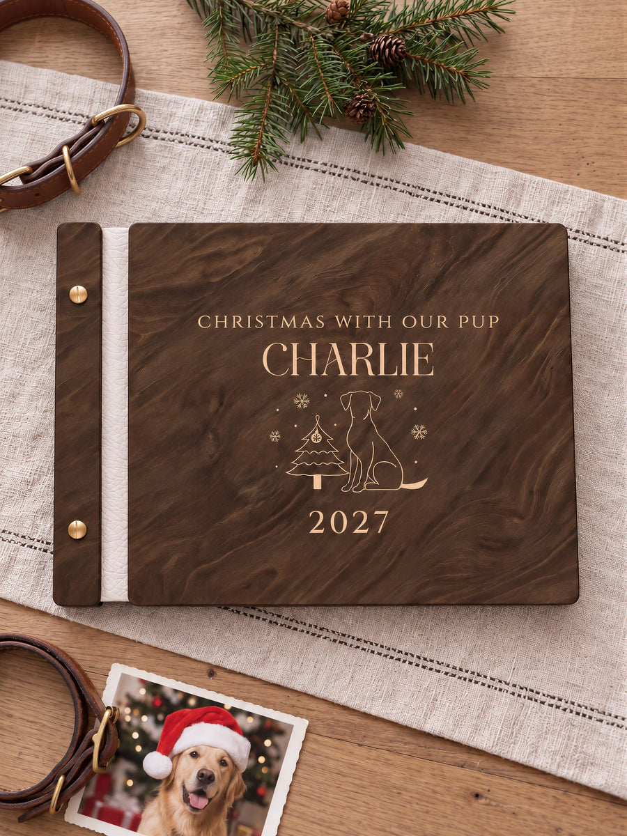 Jacobean wooden album with cream laser engraving of dog beside Christmas tree and snowflakes. The full personalized cover rests on a styled surface, with ivory binding and gold screws.