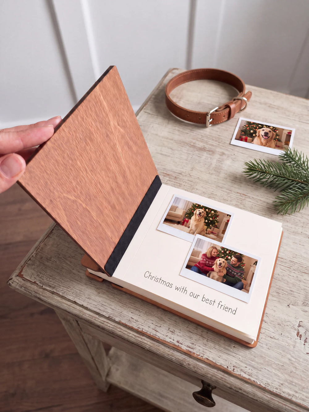 A hand lifts the Hazelnut album’s front cover, revealing a flat black inner fabric strip and a cream page arranged with instant photographs and a handwritten memory.