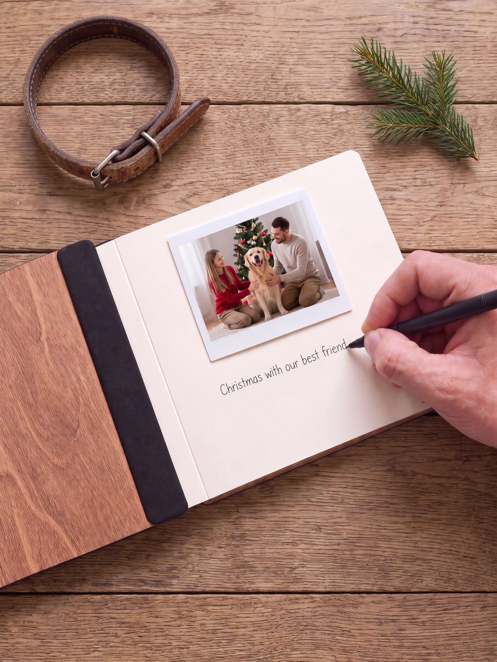 An open Hazelnut album with a photograph on a cream page. A hand writes a memory beneath it; a flat black fabric strip runs along the inner wooden cover.