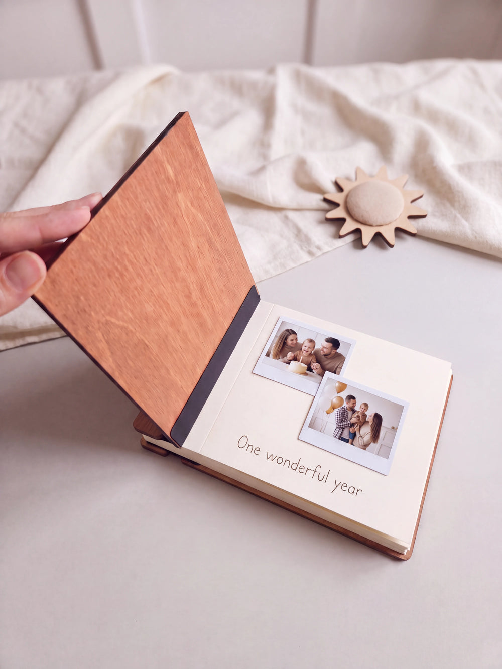 The Hazelnut first birthday photo guest book open on a table with instant photos and a short handwritten note on a cream page; the black hinge strip is visible