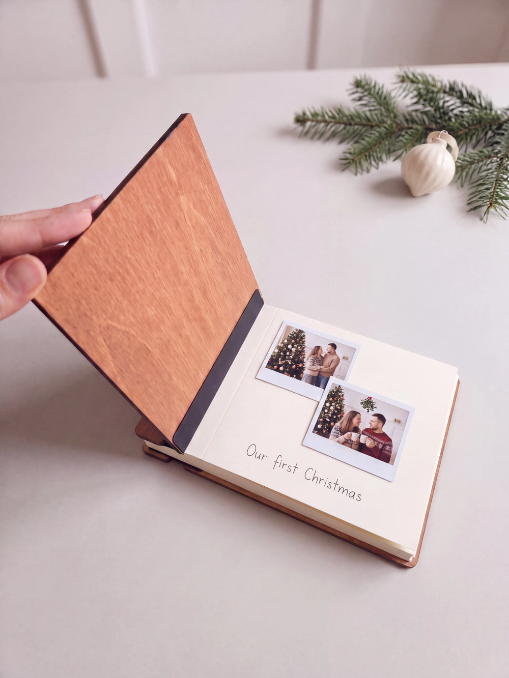 The Hazelnut First Christmas as a married couple photo book open on a table with instant photos and a short handwritten note on a cream page; the black hinge strip is visible
