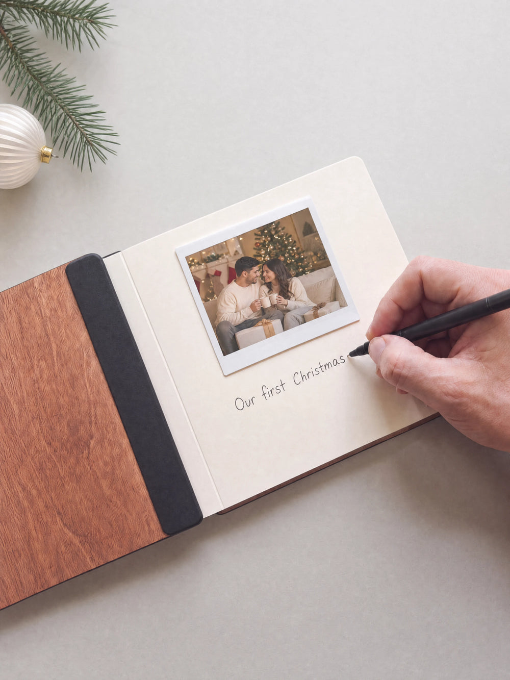 A hand writing a note in fine black pen beneath an instant photo on the cream page of the open Hazelnut First Christmas as a married couple photo book