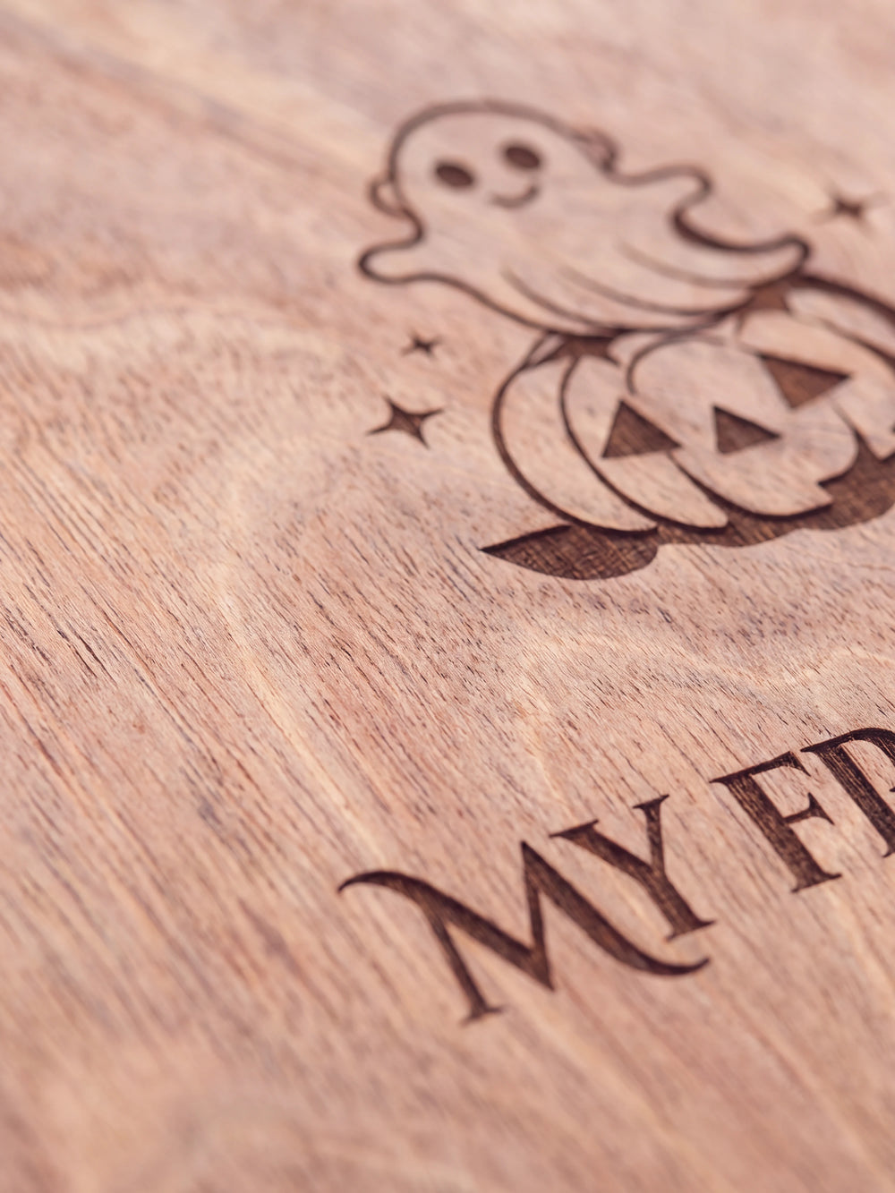 Close-up of the laser engraving on Hazelnut wood: a friendly ghost sitting on a smiling pumpkin and the personalized text against the visible wood grain