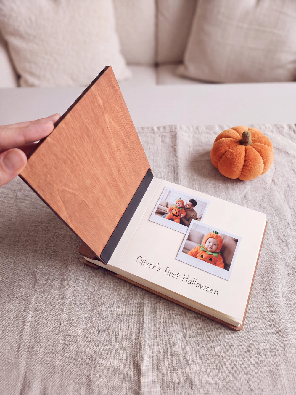 The Hazelnut My First Halloween keepsake book open on a table with instant photos and a short handwritten note on a cream page; the black hinge strip is visible