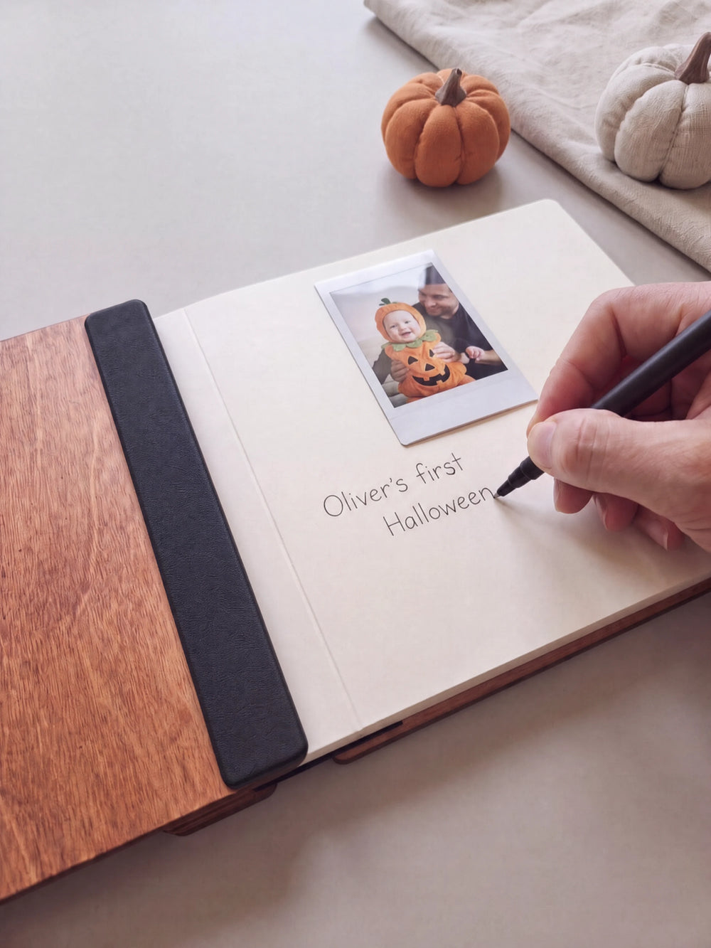A hand writing a note in fine black pen beneath an instant photo on the cream page of the open Hazelnut My First Halloween keepsake book