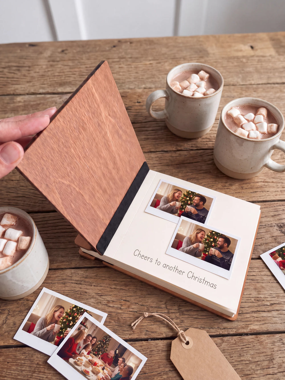 A hand lifts the Hazelnut album’s front cover, revealing a flat black inner fabric strip and a cream page arranged with instant photographs and a handwritten memory.