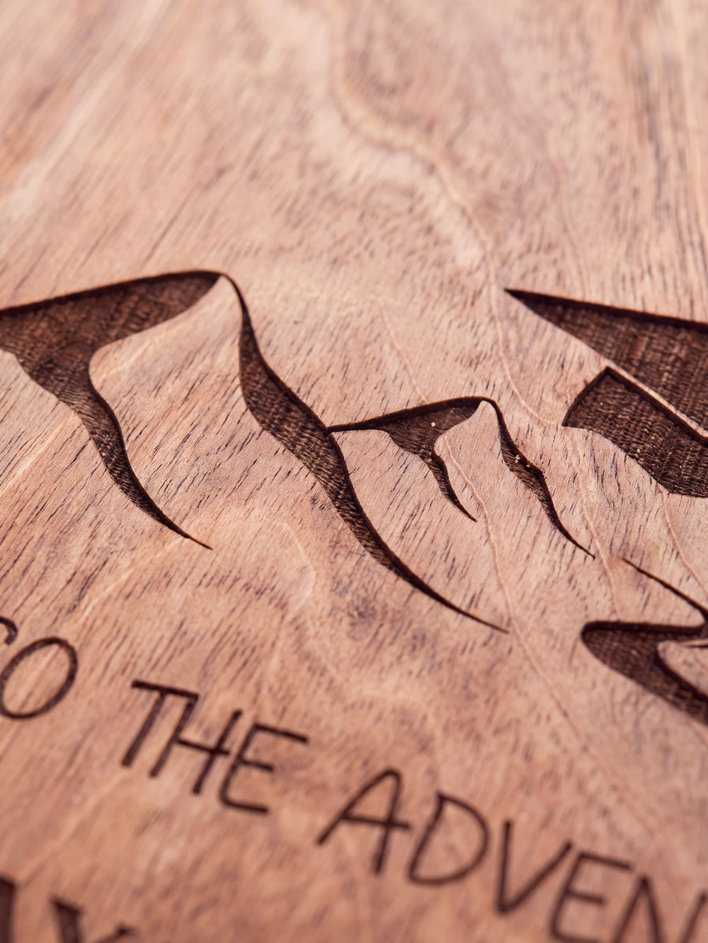 Close-up of the laser engraving on Hazelnut wood: mountain peaks beneath a graduation cap and the personalized text against the visible wood grain