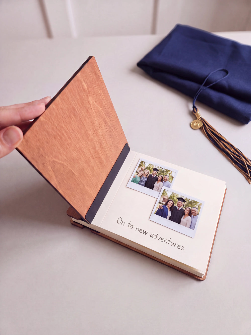 The Hazelnut graduation photo guest book open on a table with instant photos and a short handwritten note on a cream page; the black hinge strip is visible