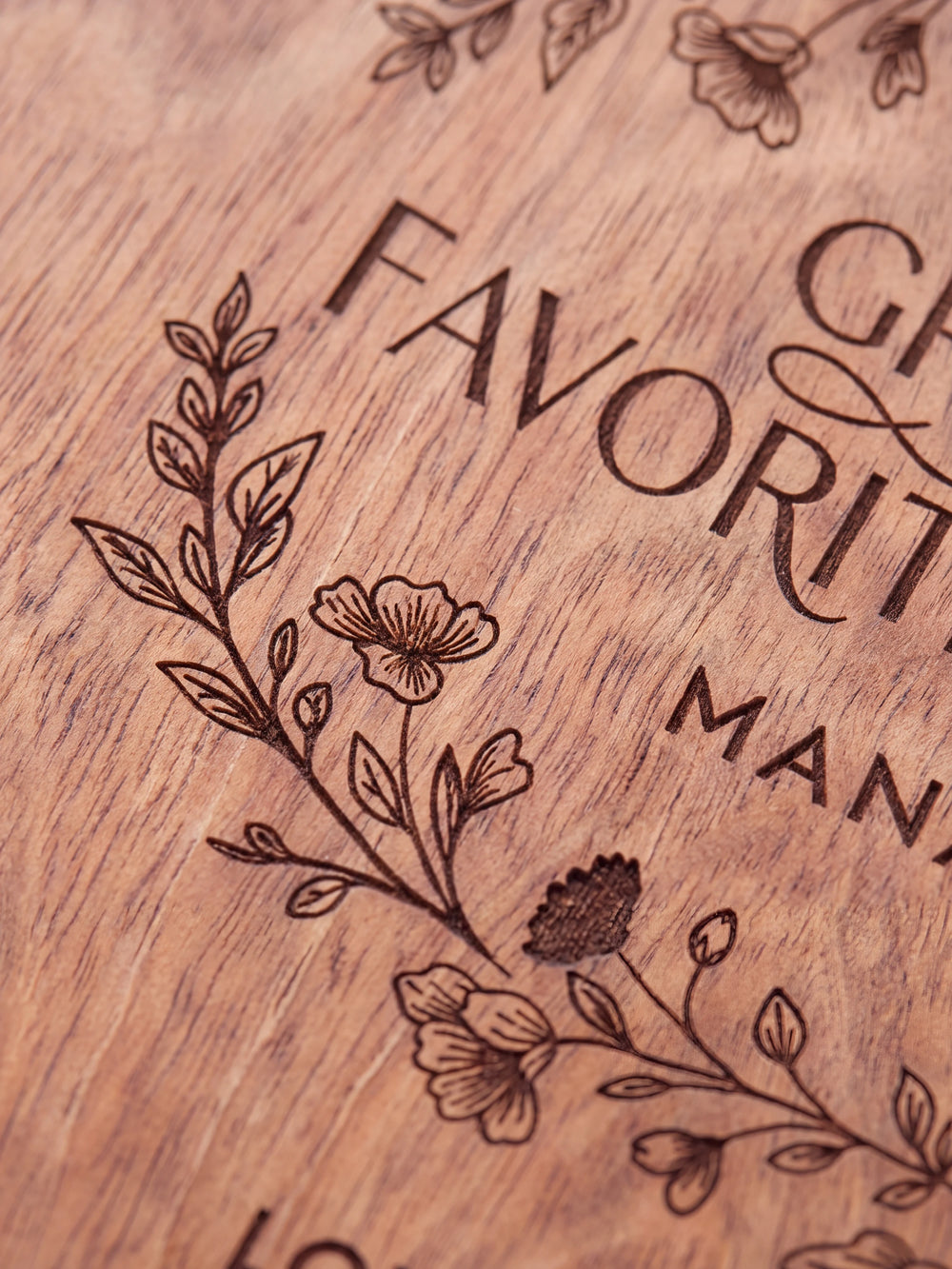 Close-up of the laser engraving on Hazelnut wood: an oval botanical wreath with small berries and the personalized text against the visible wood grain
