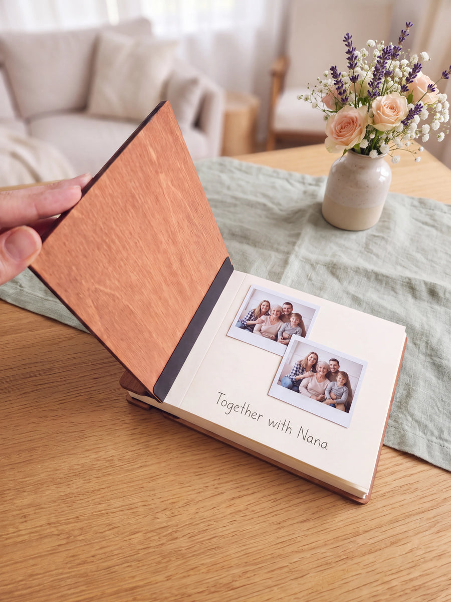 Open wooden-covered photo guest book with instant photos and a handwritten note on a cream page