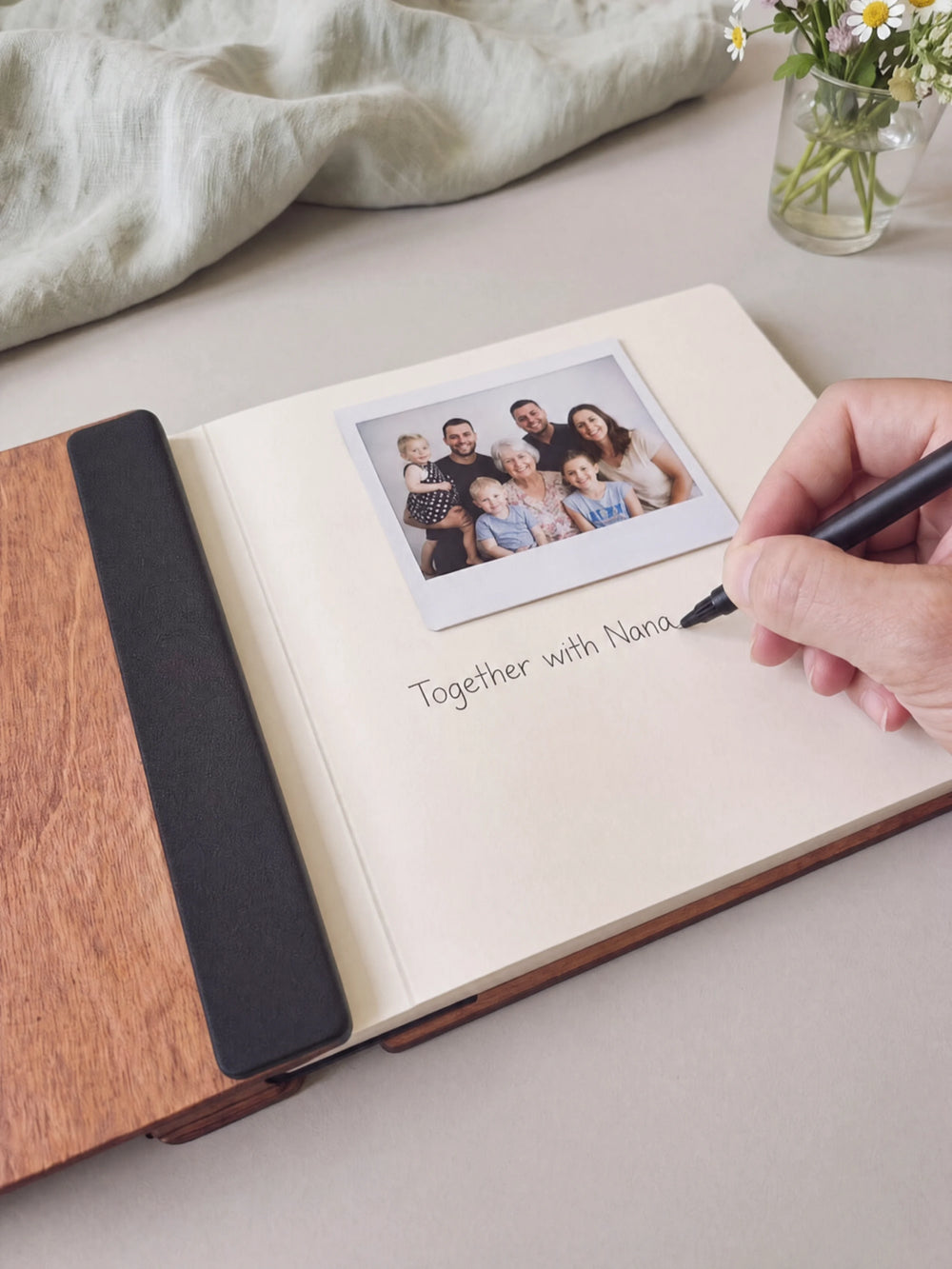 A hand writing a note in fine black pen beneath an instant photo on the cream page of the open Hazelnut Grandma's Favorite Memories photo book