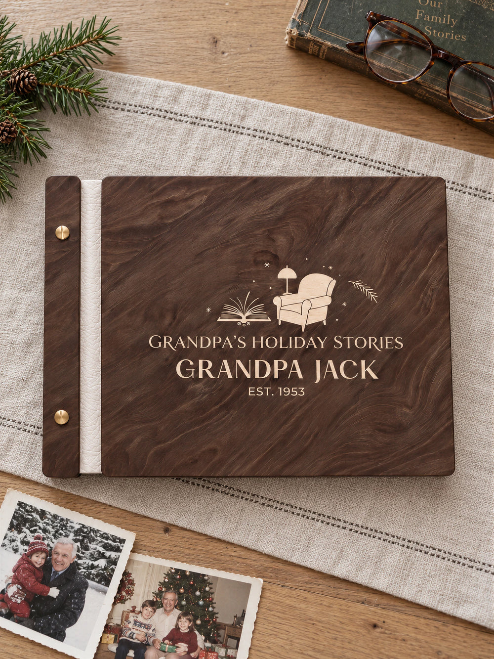 Jacobean wooden memory book with cream laser engraving, ivory binding and gold screws on a linen runner. Reading glasses, a worn storybook and family holiday snapshots surround the full cover.
